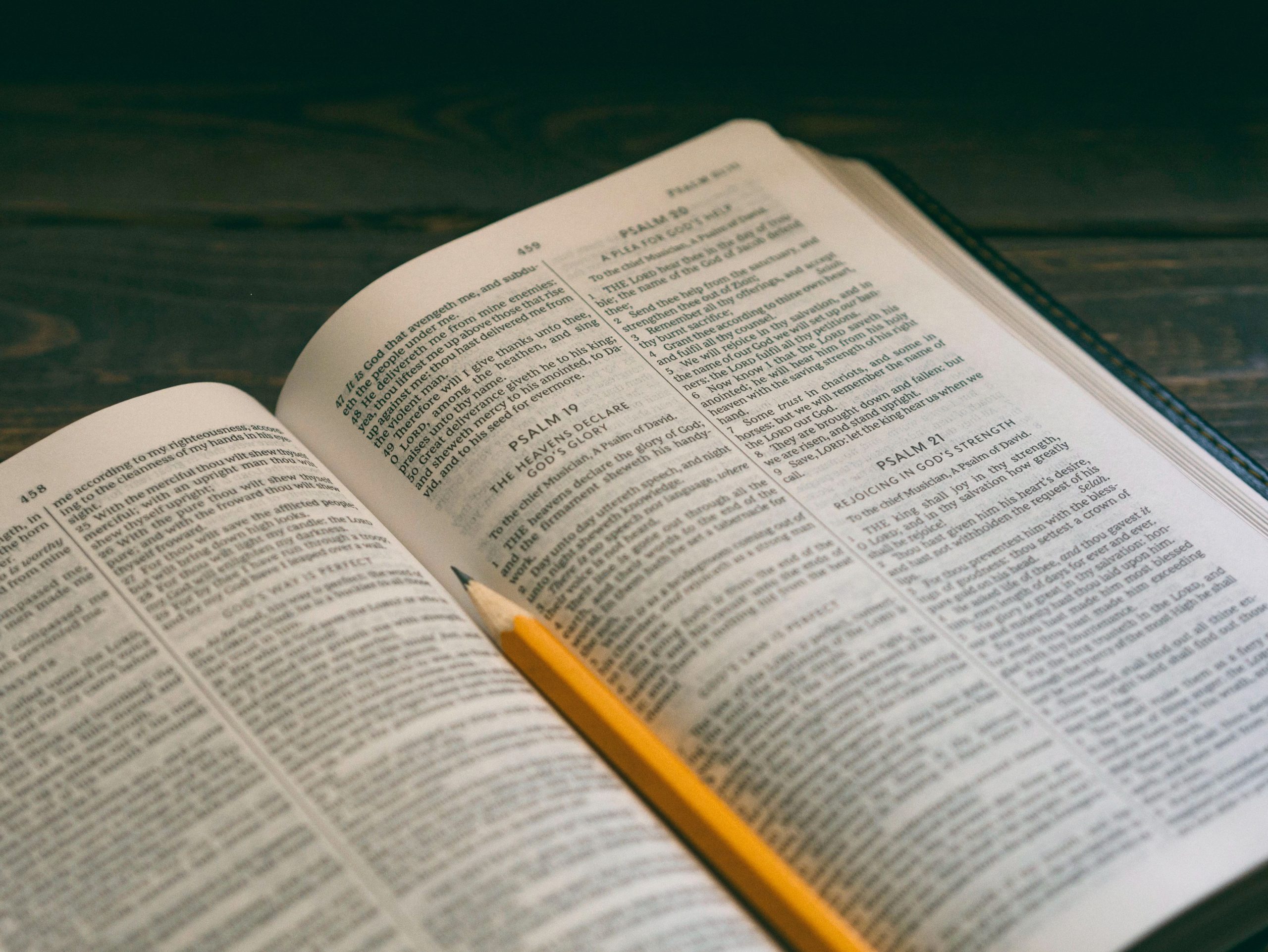 Bible open to Psalms with sharp pencil, on a dark wood table